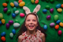 Retrato de uma menina vestindo orelhas de coelho deitado no chão cercado por ovos de Páscoa — Fotografia de Stock