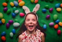 Portrait of a girl wearing bunny ears lying on the floor surrounded by Easter eggs — Stock Photo