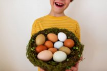 Retrato de un niño feliz sosteniendo un nido con huevos frescos - foto de stock