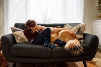 Boy lying on couch cuddling golden retriever dog — Stock Photo