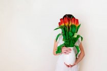 Retrato de niña sosteniendo jarrón de tulipanes - foto de stock