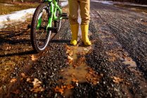 Gros plan d'un garçon portant des bottes wellington debout près de son vélo, États-Unis — Photo de stock