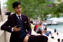 Young Businessman sitting on riverwalk holding his mobile phone, Chicago, Illinois, United States — Stock Photo