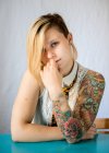Портрет жінки з татуюванням на рукаві сидить за столом — стокове фото