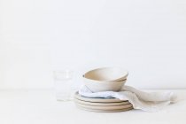 Stapeln von keramischen Tellern und Schalen neben einem Glas Wasser — Stockfoto