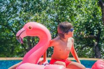 Boy sitting on an inflatable flamingo in a swimming pool, Bulgaria — Stock Photo