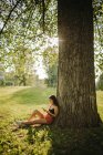 Mujer sentada bajo un árbol mirando su teléfono móvil, Serbia - foto de stock