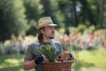 Ritratto di un uomo in piedi in un giardino con un cesto pieno di attrezzi da giardinaggio, Germania — Foto stock