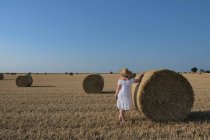 Mujer de pie en un campo apoyado sobre un heno Bale, Francia - foto de stock