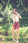Joyeux garçon debout dans le jardin jouant avec un tuyau d'arrosage en été, Espagne — Photo de stock