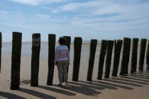 Frau steht am Strand und blickt durch Holzpfosten, Calais, Pas-de-Calais, Frankreich — Stockfoto
