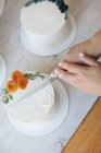 Frau schneidet Kuchen mit Buttercremeglasur und Pfirsichen — Stockfoto