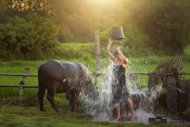 Frau steht auf einem Feld und schüttet sich einen Eimer Wasser über den Kopf, Thailand — Stockfoto