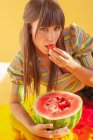 Porträt einer lächelnden Frau, die auf holographischer Folie liegt und Wassermelone isst — Stockfoto