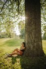 Mujer sentada bajo un árbol mirando su teléfono móvil, Serbia - foto de stock