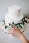 Mulher decorando um bolo de casamento de duas camadas com ramos de oliveira — Fotografia de Stock