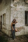 Jeune femme élégante dans des lunettes de soleil posant par vieux mur de bâtiment — Photo de stock