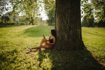 Femme assise sous un arbre regardant son téléphone portable, Serbie — Photo de stock