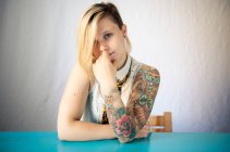 Portrait of a woman with a sleeve tattoo sitting at a table — Stock Photo