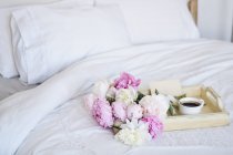 Bouquet of peonies and a cup of coffee with an envelope on a tray on a bed — Stock Photo