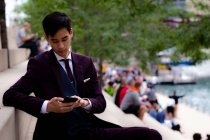 Молодой бизнесмен, сидящий на берегу реки, глядя в свой мобильный телефон, Чикаго, штат Иллинойс, США — стоковое фото