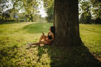 Жінка сидить під деревом і дивиться на свій мобільний телефон (Сербія). — стокове фото