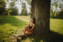 Mujer sentada bajo un árbol en el parque, Serbia - foto de stock