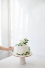Жінка прикрашає дворівневий весільний торт з оливковими гілками — стокове фото