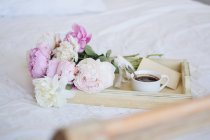 Buquê de peônias e uma xícara de café com um envelope em uma bandeja em uma cama — Fotografia de Stock