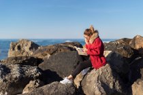 Woman sitting on rocks by the sea reading a book, Emilia Romagna, Italy — Foto stock