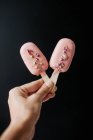 Mão de mulher segurando dois sorvetes Bolo pops decorados com polvilhas e pétalas de rosa — Fotografia de Stock