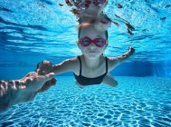 Девушка плавает под водой в бассейне с помощью своего отца — стоковое фото