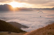Vista a distanza di persona che vola su paracadute in un paesaggio montuoso con nuvole basse — Foto stock
