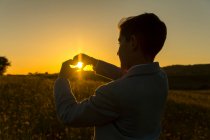 Junge, der bei Sonnenuntergang mit seinen Händen ein Herz in Form bringt, Spanien — Stockfoto