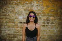 Portrait of smiling young woman standing in front of brick wall — Stock Photo