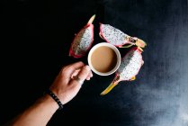 Mano de hombre sosteniendo una taza de té y cuñas de fruta de dragón - foto de stock