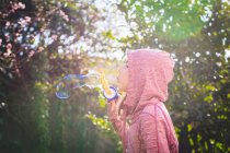 Хлопчик стоїть в саду і дме мильні бульбашки — стокове фото