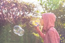 Мальчик, стоящий в саду и дующий мыльные пузыри — стоковое фото