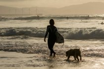 Silhouette einer Surferin, die mit ihrem Hund in der Brandung geht, Bilbao, Spanien — Stockfoto