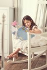 Mädchen sitzt im Schaukelstuhl und liest ein Buch — Stockfoto