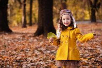 Chica sonriente de pie en el parque sosteniendo una hoja, Bulgaria - foto de stock