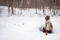 Хлопчик в зимовому одязі, вкритому снігом, грає зі снігом в парковій сцені — стокове фото