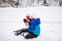 Junge sitzt auf gefrorenem See und isst Schnee, Wisconsin, Vereinigte Staaten — Stockfoto