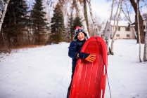 Boy standing in a garden with his sledge, Wisconsin, United States — Stock Photo
