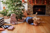 Menino abraçando com cão no interior decorado de natal — Fotografia de Stock