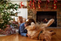 Menino abraçando com cão no interior decorado de natal — Fotografia de Stock