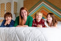 Мати і троє дітей лежать на ліжку посміхаючись — стокове фото