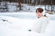 Retrato de una niña con orejeras de unicornio de pie en un fuerte de nieve, Estados Unidos - foto de stock