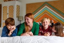 Mãe e três filhos deitados na cama sorrindo — Fotografia de Stock