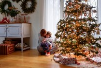 Mãe e filho abraçando pela árvore de natal em casa — Fotografia de Stock